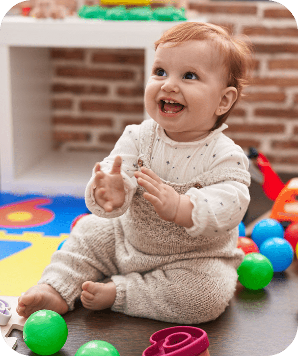 Smiling baby sitting among colorful toys.